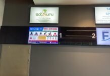 SLCAA DG Assures Public of Robust Ebola Preparedness at Freetown International Airport Airport interior with multiple backlit signs: SatSuru Travel logo, an Ebola screening poster, and numbered gates 1 and 2 on a dark wall panelage beside a doorway.