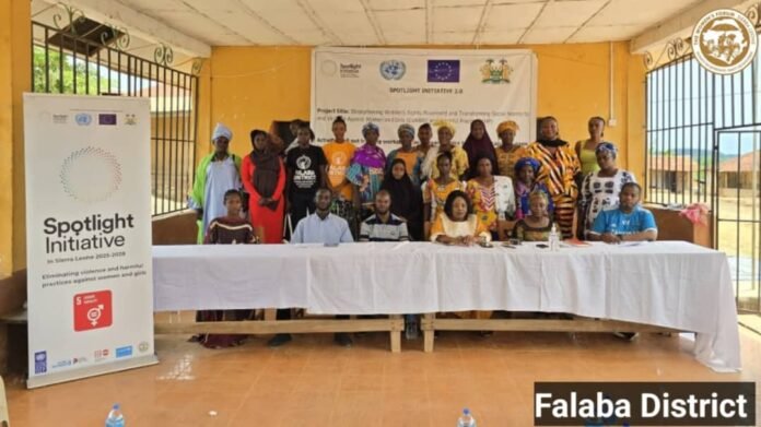 Group of men and women posing for a photo at a community event with a Spotlight Initiative banner in the background, Falaba District.