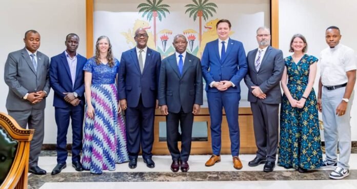 Nine professionals in formal attire pose for a group photo in a reception area, with a palm mural behind them on the wall.