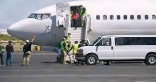 Passengers boarding a small commercial jet via portable stairs on the tarmac, with ground crew and a white service van nearby.