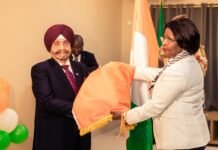 Mohinder Bir Singh Sachdeva Assumes Office as Côte d’Ivoire’s Honorary Consul in Sierra Leone Two formally dressed individuals exchange a folded orange flag during a ceremony, with balloons in the background.