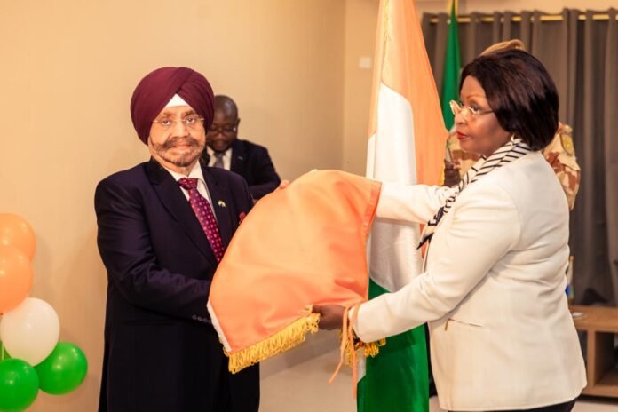 Two formally dressed individuals exchange a folded orange flag during a ceremony, with balloons in the background.