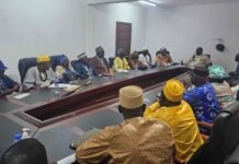 NCRA Mobilizes Tribal Heads to Expand National Identification Coverage Group of people in traditional attire seated around a long conference table in a meeting room, engaged in discussion with papers and water bottles on the table.