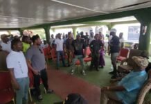 Hon. Alhaji Musa Tarawally Secures NaCoS Endorsement Ahead of 2028 Elections A group of people standing and mingling in a covered outdoor hall with green pillars and red chairs.
