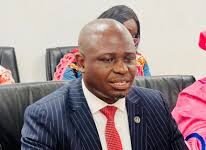 Opposition Leader Raises Red Flag Over Sierra Leone’s Growing Drug Trafficking Reputation Man in a navy pinstripe suit and red tie sits at a conference table with a red bottle, smartphone, and papers in front of him in a meeting room.