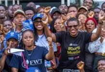 DortiMusGo Initiative Takes Effect as FCC, Police Sign Enforcement Pact Diverse crowd at a rally, smiling and posing for the camera with raised fists in casual clothing, showing solidarity.