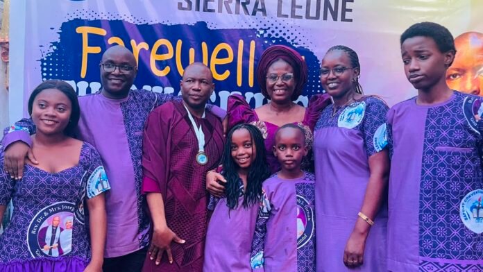 Group of eight people in matching purple outfits posing for a farewell event in front of a banner that reads 'Farewell'.