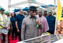 President Bio Commissions Historic 40MW Solar Power Projects, Declares New Chapter in Energy Transformation Man in a gray suit and black hat speaks into a microphone at an outdoor ceremony, surrounded by officials on a red carpet with a crowd behind.