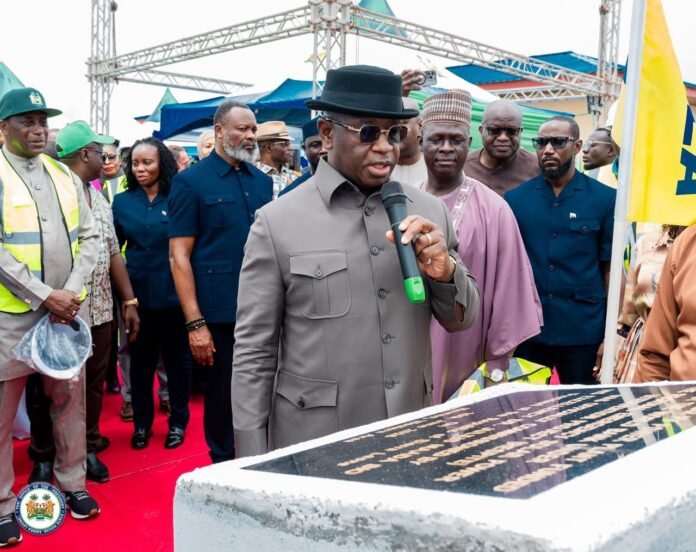 President Dr. Julius Maada Bio Man in a gray suit and black hat speaks into a microphone at an outdoor ceremony, surrounded by officials on a red carpet with a crowd behind.