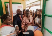 Orange Sierra Leone Foundation, Partners Boost Maternal Healthcare in York Community A ribbon-cutting ceremony at a doorway, with a woman in pink cutting the ribbon while a crowd cheers and records the moment.