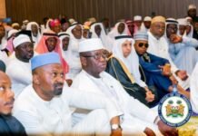 Vice President Hails Seamless 2026 Hajj, Praises President Bio’s Leadership A large crowd of men in white traditional dress seated in a conference hall; central figure wears glasses and a white cap.