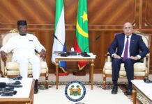 ECOWAS Chair, Mauritanian President Reaffirm Commitment to Regional Peace, Security and Cooperation Two men in formal attire sit in ornate chairs across from each other in a wood-paneled room, with flags and microphones on a table between them and a presidential emblem on the floor nearby.