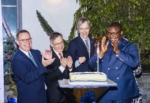 EU, Sierra Leone Celebrate 50 Years of Strategic Partnership and Development Cooperation Four men in suits clap and smile around a cake with a lit candle at a celebration event.