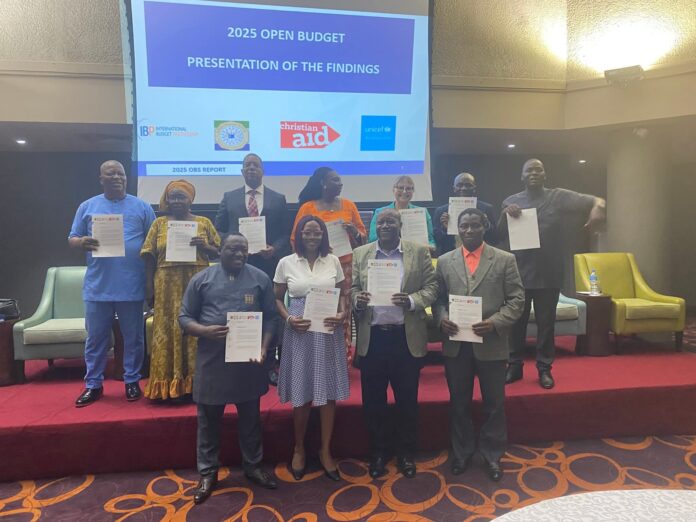 Group of people on a stage holding certificates, posing for a photo during a budget presentation event, with a slide showing '2025 OPEN BUDGET' in the background.