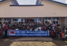 China’s Medical Team Hosts Health and Charity Event in Freetown for International Day of the African Child Group photo of a large medical team and local people in front of a building, holding a banner that reads 'China Medical Team to Sierra Leone'.