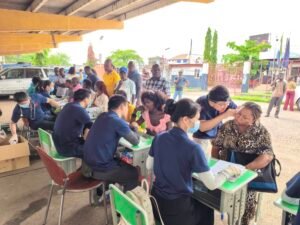 Medical volunteers vaccinating people at an outdoor clinic under a yellow covered area.