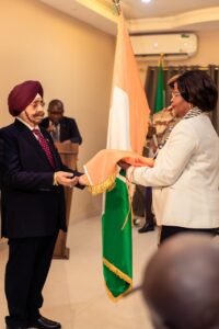 A formal flag ceremony: a man in a turban hands a peach shawl to a woman in a light suit, with the Ivory Coast flag nearby.