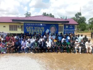 | The Calabash Newspaper Group of people posing in front of a building with a blue banner that says 'Get Your Resident Permit'.