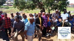 | The Calabash Newspaper Group of people gathered outdoors under a tree for a community event, with a Sustainability Broadcasting logo in the corner.