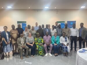 Diverse group of adults posing for a formal group photo in a conference room, with UNICEF banners visible in the background.
