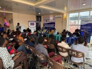 Panel discussion at a community workshop with attendees seated facing the speakers; event banners in the background.