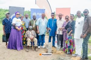 Group of diverse people at a groundbreaking ceremony outdoors, some with shovels, standing in front of banners with Foundation logos.