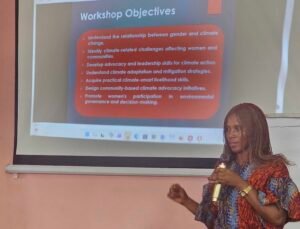 Presenter with microphone speaks next to a slide titled 'Workshop Objectives' in a classroom setting.