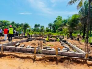Construction workers in high-visibility vests lay concrete foundations on a sunny tropical site.