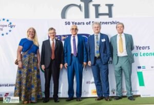 Five people in business attire standing in a row for a group photo at a corporate event, with a banner saying '50 Years of partnership' in the background.