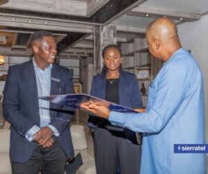 | The Calabash Newspaper Three professionals in business attire review a document together in a modern office lobby setting with seating behind them.