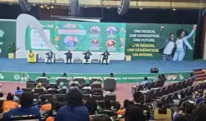 Panel discussion on a large stage with five speakers seated in white chairs; banner reads 'One Region. One Generation. One Future.'
