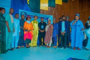 | The Calabash Newspaper Group of people on a stage posing for a photo at a colorful event, wearing bright traditional outfits and robes.