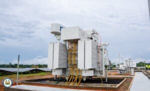Large electrical transformer unit on a concrete pad at a solar farm, with yellow cables and overhead wiring nearby.