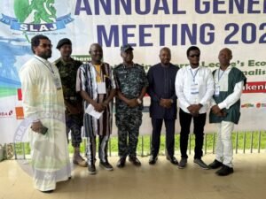 | The Calabash Newspaper Seven men in varied traditional, business, and military outfits pose for a group photo at an event, in front of a banner that reads 'Annual General Meeting 2021'