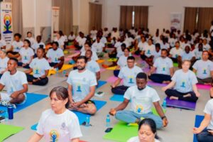 Group of people meditating in a large hall on colorful yoga mats, all wearing white event shirts with a logo(s). felt calm atmosphere.