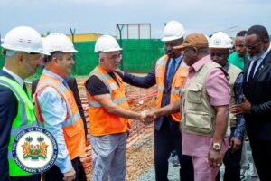 Group of officials in hard hats and safety vests shaking hands at a construction site.