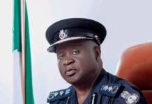 Guild of Newspaper Editors Condemns Police Visit to Voice of Salone Office Portrait of a Sierra Leone police officer in uniform seated at a desk with folded hands, flag in the background.