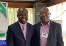 African Climate Platform Commends Sierra Leone’s Ratification of African Court Protocol Two smiling men in business suits posing together at a conference, one with a pink striped tie and the other with a name badge on his lapel.
