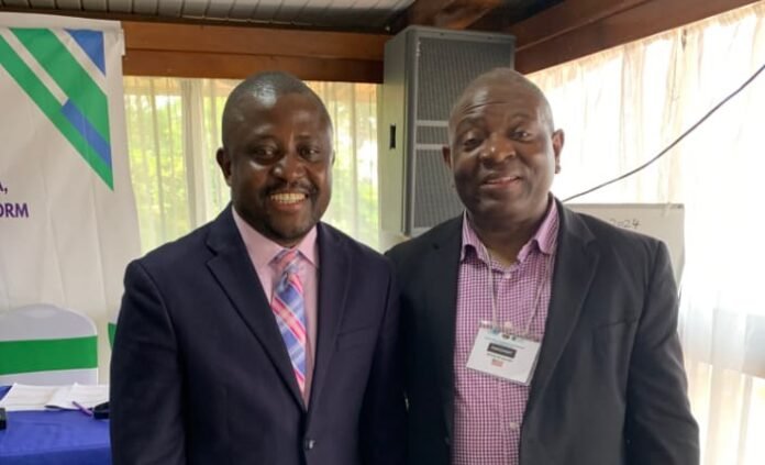 Two smiling men in business suits posing together at a conference, one with a pink striped tie and the other with a name badge on his lapel.