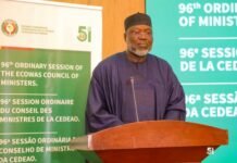 ECOWAS Commends Sierra Leone’s Security Leadership for Peaceful, Well-Coordinated Regional Programme Man in a dark purple traditional outfit speaks at a wooden podium during the ECOWAS Ministers' 96nd Ordinary Session, with banners in the background.