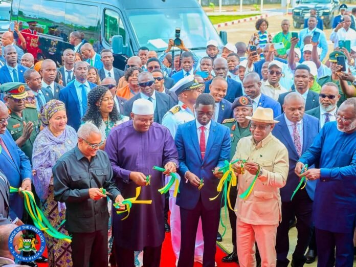Dignitaries and officials cut yellow-and-green ribbons at an outdoor ceremony, with a crowd and a blue van in the background.