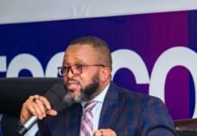 NaTCA DG Educates Consumers on Staying Safe From Fraudulent Internet Links Bearded man in a blue plaid suit speaks into a handheld microphone at a conference panel, with a water bottle and nameplate on the table in front of him.