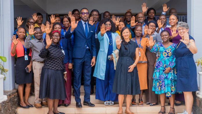Group of diverse colleagues smiling and waving from a doorway, celebrating together.