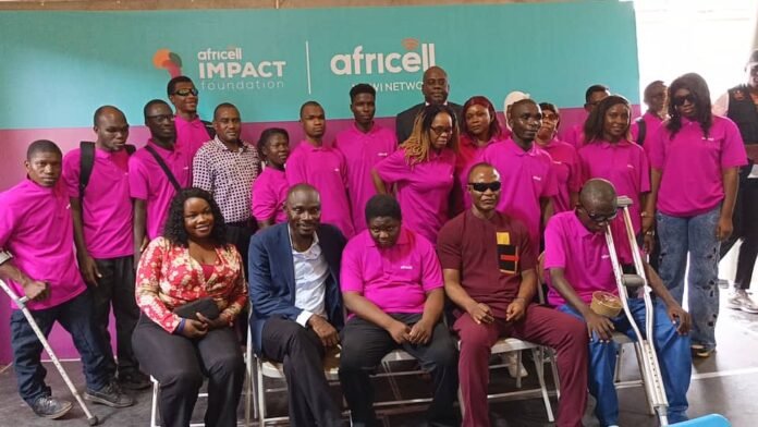 Group of people in pink shirts posing for a photo at Africell Impact Foundation event, with a turquoise backdrop behind them.