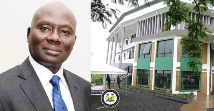 Portrait of a man in a gray suit and blue tie on the left, next to a modern white building with green-framed windows on the right, featuring a circular seal near the entrance.