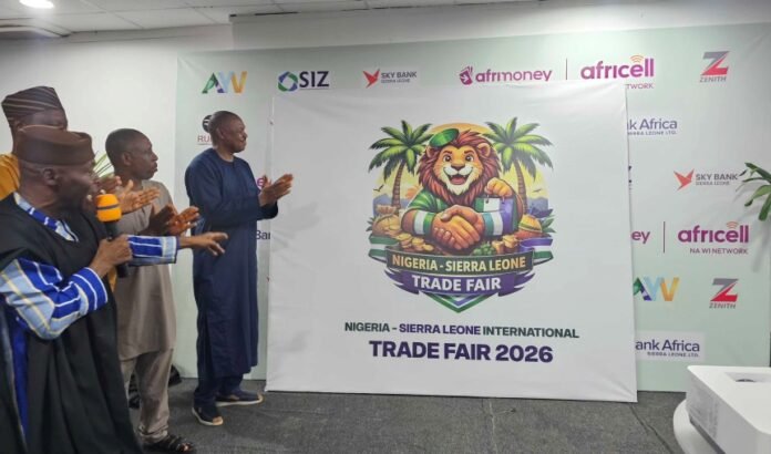 Group of men standing and clapping beside a banner featuring a lion mascot and 'Nigeria-Sierra Leone International Trade Fair 2026'.