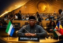 Foreign Minister Seeks AU Support on Xenophobia and ICJ Bid for Professor Charles Jalloh Sierra Leone delegate seated at a conference table with a 'SIERRA LEONE' nameplate and national flags, at a large international summit.