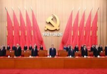 105 Years of the Communist Party of China: A Century of Transformation and a Vision for Shared Development Official ceremony with a large gold hammer-and-sickle emblem and the dates 1921–2026, surrounded by red banners and officials at a long dais.