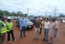 Foreign Engineers Assess Freetown’s Waste System Ahead of Infinitum Energy’s 30MW Waste-To-Energy Group of professionals standing in a construction site, some wearing safety vests and hard hats, conversing near a parked SUV.