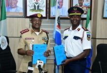 SLRSA-FRSC Five-Year Agreement Sets New Standard for Road Safety Collaboration in ECOWAS Two uniformed officials stand side by side in a conference room, each holding blue documents as microphones sit on the table in front; flags and framed portraits hang on the wall behind them.